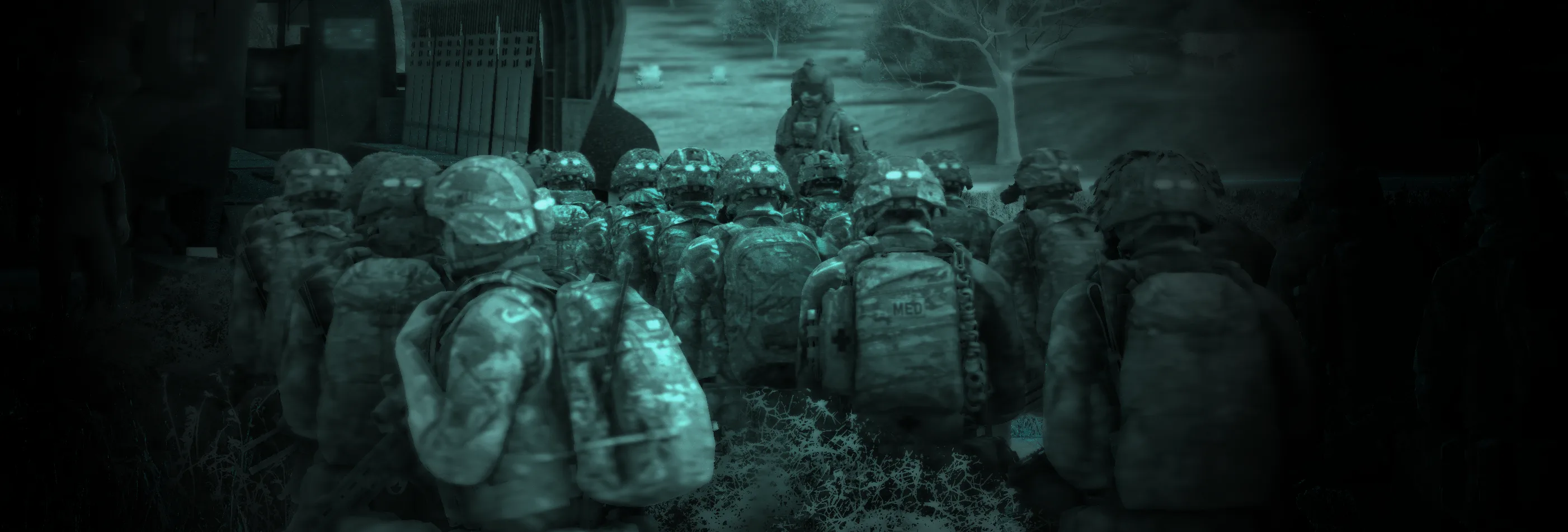 Night-vision, green-toned view of a column of soldiers with bergens moving off from a compound at night.